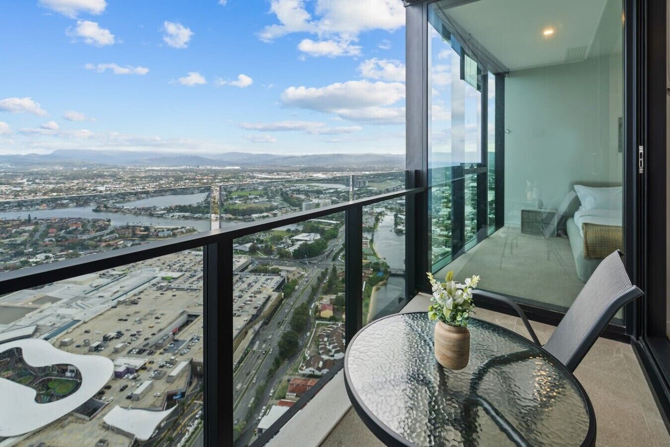 Habitación en un edificio alto con balcón de vidrio que ofrece vistas a un paisaje urbano, incluyendo un río y autopistas.