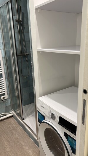 Ein Waschraum mit einer Siemens Waschmaschine, einer Duschkabine aus Glas und einer weißen Regaleinheit.