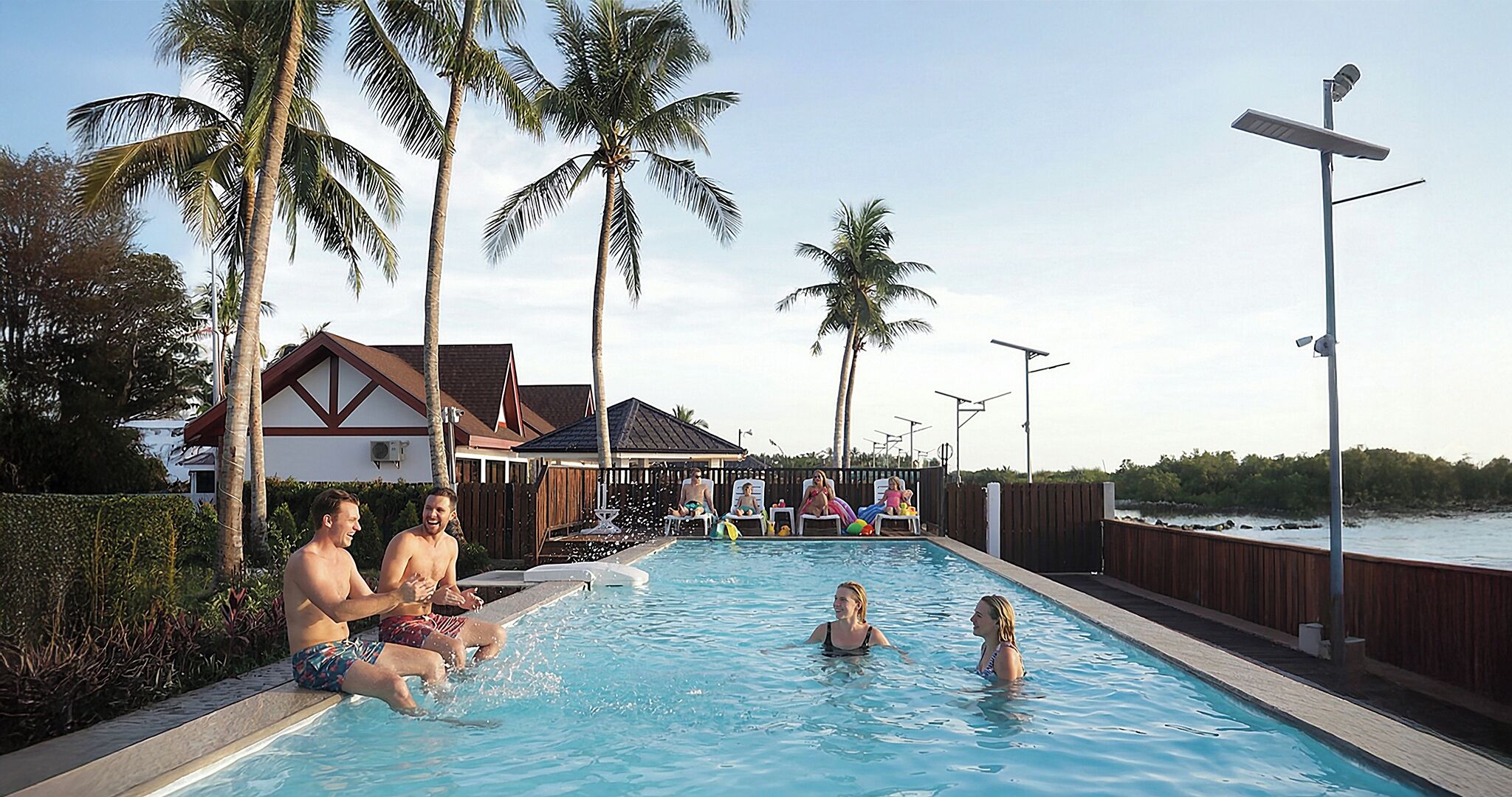 A swimming pool with people, palm trees, and a house in the background.