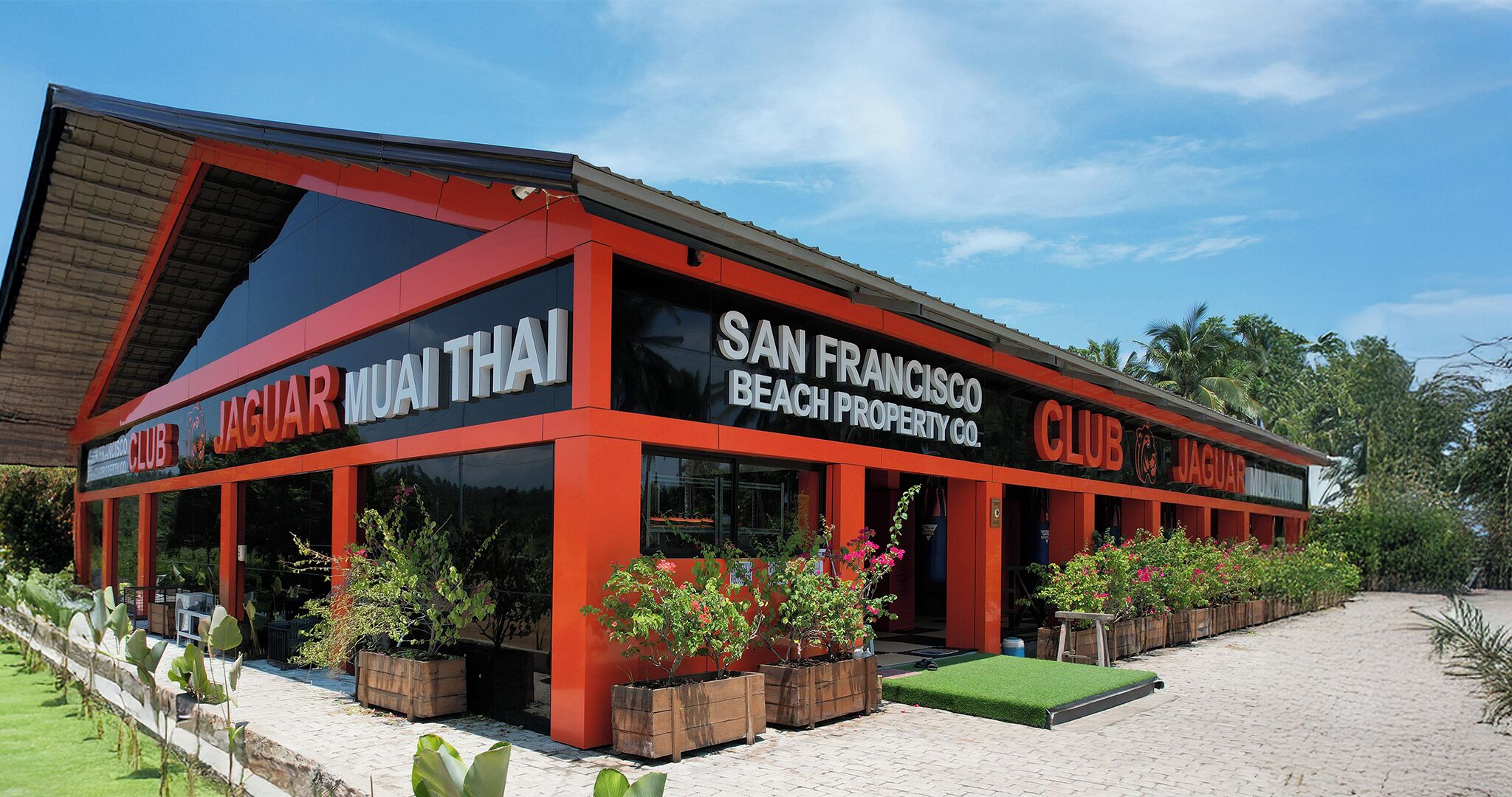 A building with 'JAGUAR MUAI THAI CLUB SAN FRANCISCO BEACH PROPERTY CO.' signage, large windows, and outdoor planters.