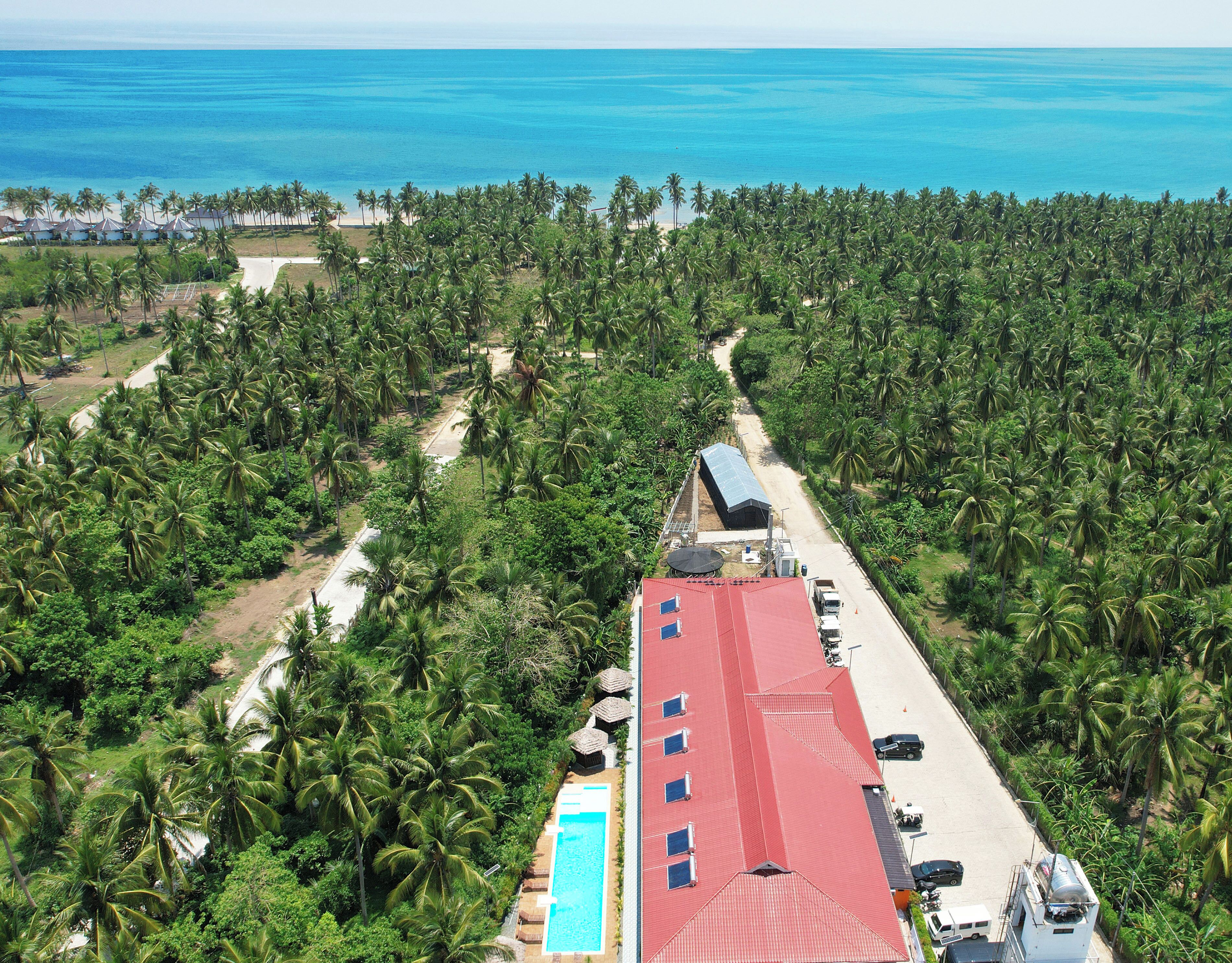 A resort with a red-roofed building, a swimming pool, and a view of the ocean.