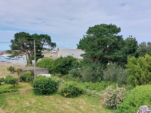 A coastal garden with dense greenery, a stone building, and a view of boats at a marina. - Ty Yannick by Interhome (Ploumanach)