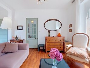 A living room with a sofa, a chair, a coffee table with a vase, a dresser, a mirror, and a door. - Ty Yannick by Interhome (Ploumanach)