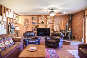 Ein gemütliches Wohnzimmer mit Ledersofas, einem Flachbildfernseher, einem Kamin und einer Backsteinwand.