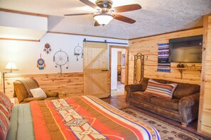 Ein gemütliches Zimmer mit Bett, einer Couch, einem Deckenventilator, einem Fernseher und einer Wand mit Traumfängern.