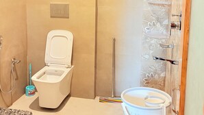 A bathroom with a toilet, shower, and a bucket. - The Kath Kuni (Kullu)