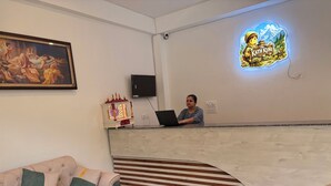A reception area with a receptionist, a framed painting, a decorative light, and a neon sign. - The Kath Kuni (Kullu)