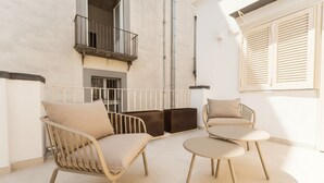 Een balkon met een bank, een kleine tafel, een raam met luiken en een balustrade.
