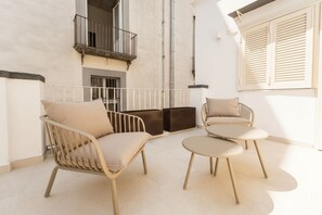 Ein Balkon mit einer Sitzecke, einem kleinen Tisch, einem Fenster mit Rollläden und einem Geländer.