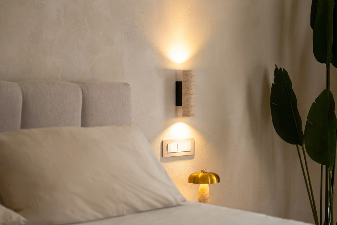 Une chambre à coucher avec un lit, une table de chevet, une lampe fixée au mur et une plante.