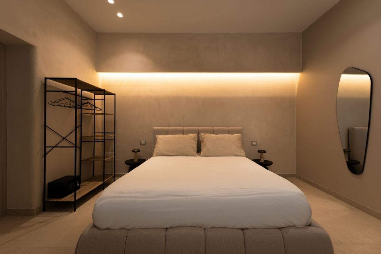 Une chambre moderne avec un grand lit, des tables de chevet, une armoire et un miroir fixé au mur.
