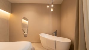 Een moderne badkamer met een vrijstaand bad, een grote spiegel en een bed met een witte dekbedsprei.