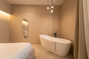 Ein modernes Badezimmer mit freistehender Badewanne, einem großen Spiegel und einem Bett mit weißer Bettdecke.