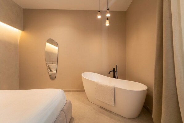 Un baño moderno con una bañera independiente, un espejo grande y una cama con cubrecama blanco.