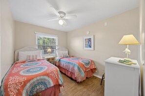 A bedroom with two beds, a ceiling fan, a window with blinds, a desk with a lamp, and a framed picture on the wall. - Short Walk to Beach | Pet-Friendly Duplex | Deck & Grill (Fernandina Beach)