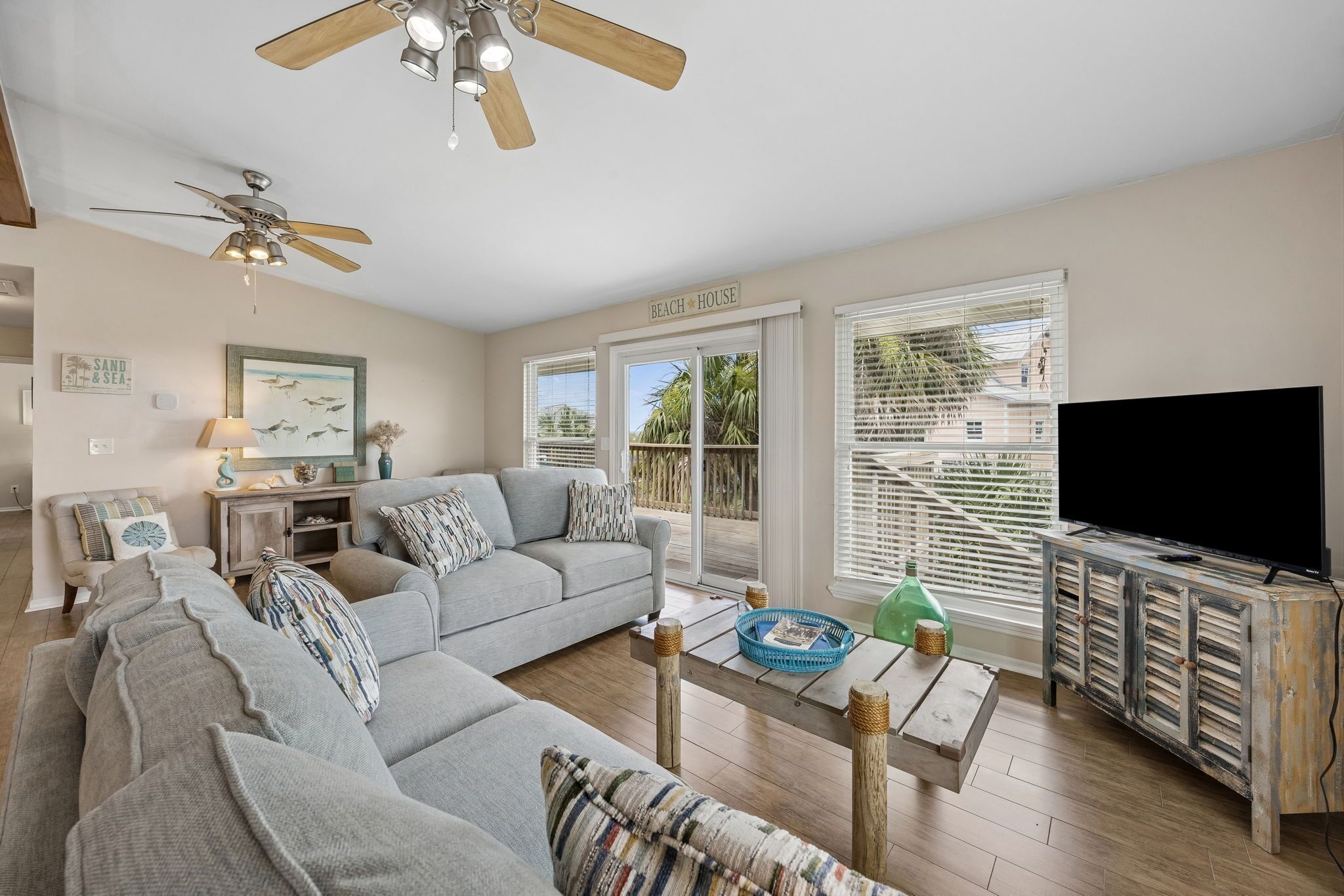 A living room with a grey sofa, a television, and a ceiling fan.