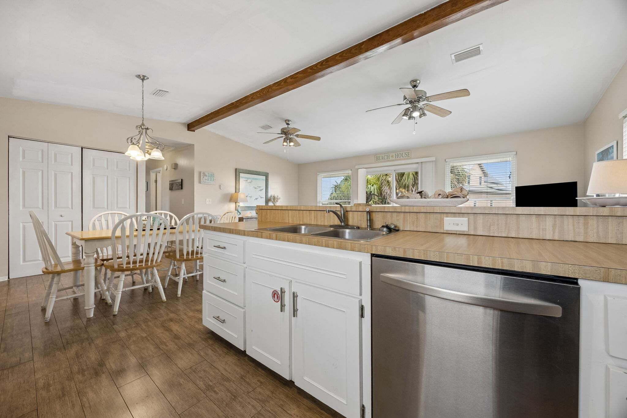 A kitchen with white cabinets, a stainless steel dishwasher, and a dining area with white chairs.
