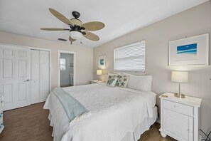 A bedroom with a bed, a ceiling fan, a nightstand with a lamp, a white dresser, and a door. - Short Walk to Beach | Pet-Friendly Duplex | Deck & Grill (Fernandina Beach)
