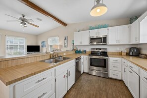 A modern kitchen with white cabinets, stainless steel appliances, a wooden countertop, and a ceiling fan. - Short Walk to Beach | Pet-Friendly Duplex | Deck & Grill (Fernandina Beach)