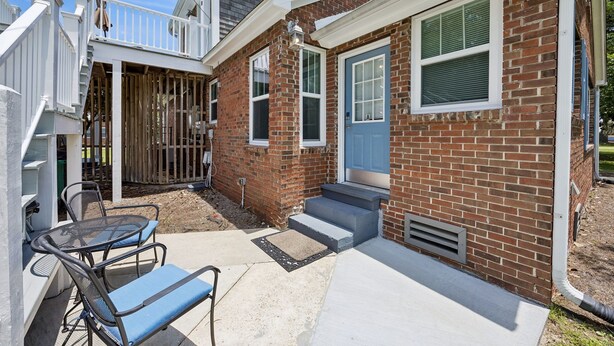 A two-story house with a front door, a small porch with a table and chairs, and a staircase leading to the upper level. - Downtown St. Marys Retreat | Sleeps 5 (St. Marys)
