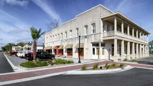 A historic building with a central entrance, a covered porch, and a street view with parked cars and a palm tree. - Downtown St. Marys Retreat | Sleeps 5 (St. Marys)