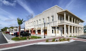 A historic building with a central entrance, a covered porch, and a street view with parked cars and a palm tree. - Downtown St. Marys Retreat | Sleeps 5 (St. Marys)