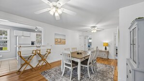 A modern kitchen with white cabinets, a dining area with a wooden table and white chairs, and a ceiling fan. - Downtown St. Marys Retreat | Sleeps 5 (St. Marys)