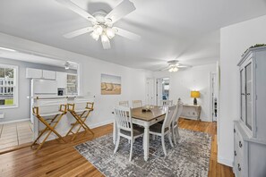A modern kitchen with white cabinets, a dining area with a wooden table and white chairs, and a ceiling fan. - Downtown St. Marys Retreat | Sleeps 5 (St. Marys)