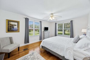A bedroom with a bed, a chair, a dresser, a ceiling fan, and large windows. - Downtown St. Marys Retreat | Sleeps 5 (St. Marys)