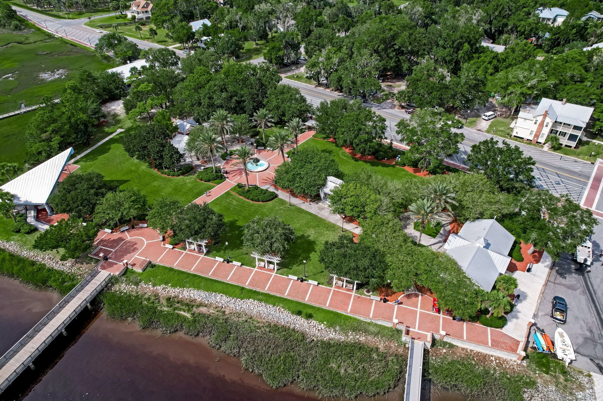 An aerial view of a residential area with a paved walkway, a bridge, and a body of water.