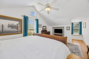 Ein Schlafzimmer mit einem großen Bett, einem Deckenventilator, einem Fernseher und einem Fenster mit Vorhängen.