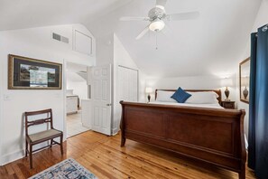 A bedroom with a wooden bed, a chair, a ceiling fan, and a door leading to another room. - Downtown St. Marys Retreat | Sleeps 2 (St. Marys)