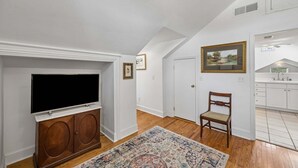 A room with a television on a wooden cabinet, a chair, a rug, and a painting on the wall. - Downtown St. Marys Retreat | Sleeps 2 (St. Marys)
