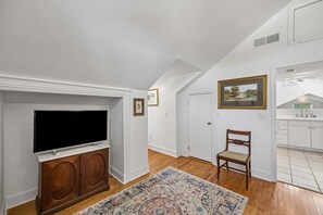 A room with a television on a wooden cabinet, a chair, a rug, and a painting on the wall. - Downtown St. Marys Retreat | Sleeps 2 (St. Marys)