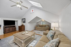 A spacious loft with a high ceiling, a ceiling fan, a large window, a flat-screen TV, a wooden entertainment unit, a beige sofa, a patterned throw pillow, a lamp, and a small table with a tray. - Downtown St. Marys Retreat | Sleeps 2 (St. Marys)