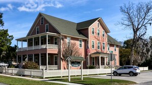 A two-story historic Spencer House Inn with a porch, a signboard, and a white picket fence. - Downtown St. Marys Retreat | Sleeps 2 (St. Marys)