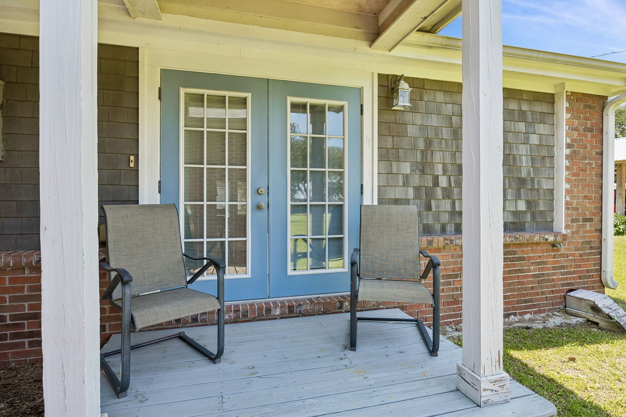 A porch with two chairs, a blue door, and a brick wall.