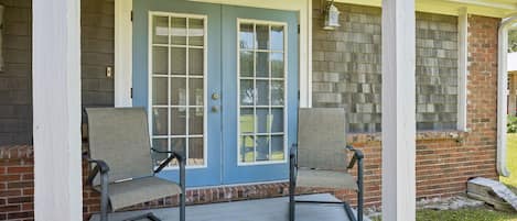 A porch with two chairs, a blue door, and a brick wall.