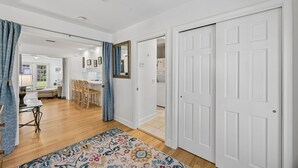 Um corredor com um tapete estampado, uma área de refeições com cadeiras e uma mesa, e uma porta branca.