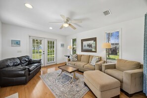 A living room with a black leather sofa, beige armchairs, a coffee table, and a ceiling fan. - Downtown St. Marys Retreat | Sleeps 2 (St. Marys)