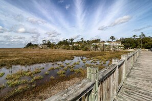 A wooden boardwalk leading to a residential area with houses and a marshy landscape. - Downtown St. Marys Retreat | Sleeps 2 (St. Marys)