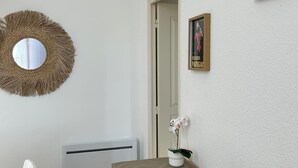 Una habitación con un espejo redondo, un cuadro enmarcado, un radiador, una mesa con una bandeja verde y una silla blanca.