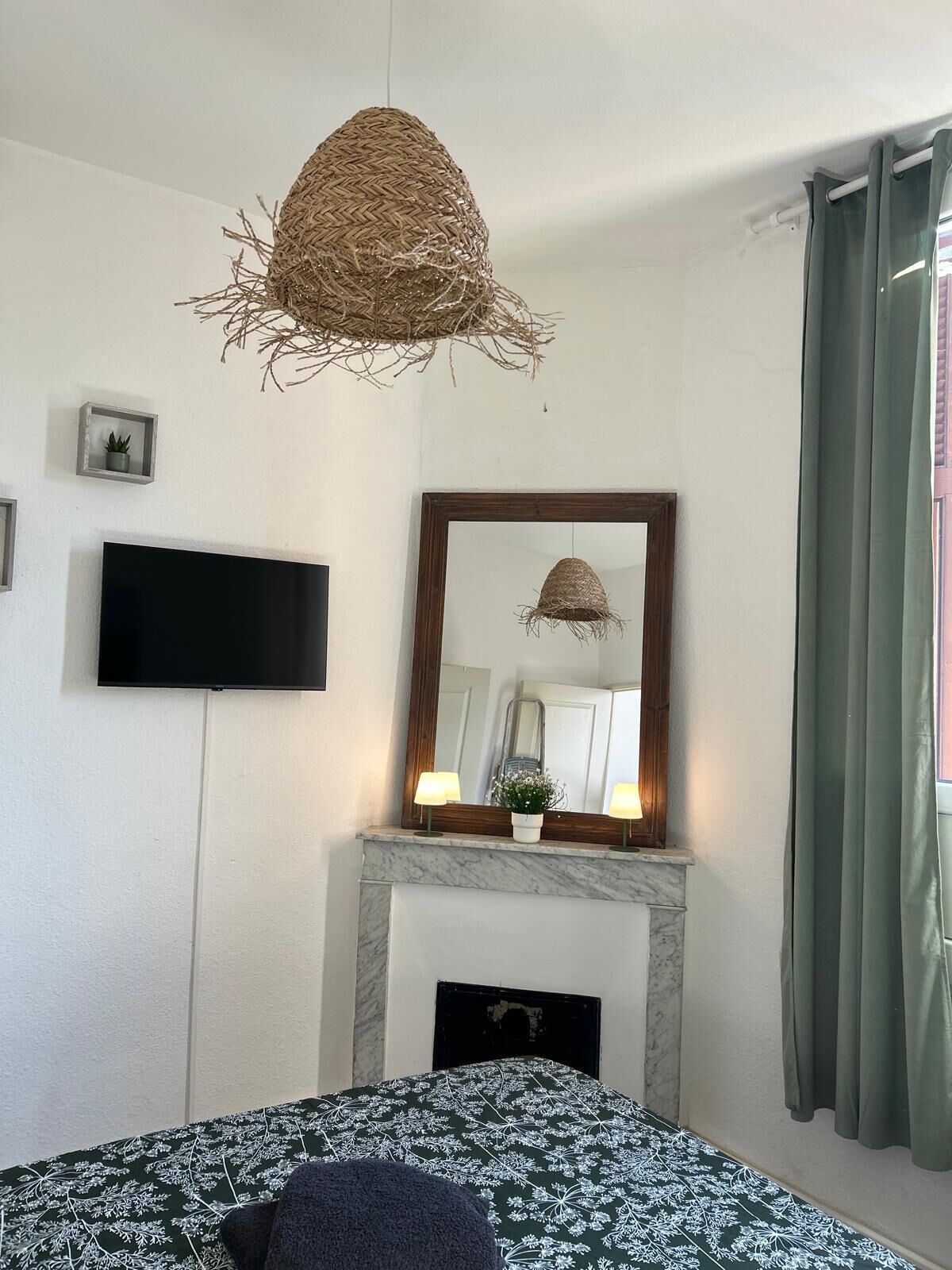 A bedroom with a bed, a television, a mirror, a fireplace, and a hanging light fixture.