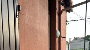 Un balcón con un pequeño área de césped artificial, barandilla de metal y fachada de edificio con superficie texturizada.