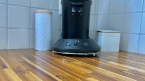 Una cafetera sobre una mesa de madera con una pared de azulejos blancos al fondo.