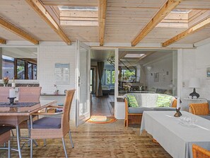 A spacious living area with a wooden floor, a dining table with chairs, a sofa, and a kitchen visible through an open doorway.