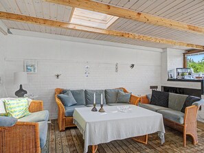 A cozy room with a white brick wall, wooden ceiling beams, a white table, wicker furniture, and a fireplace.