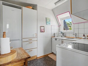 A compact kitchen with white cabinets, a wooden table, a refrigerator, a dishwasher, and a window with a view. - "Rosalie" - 150m from the sea by Interhome (Otterup)