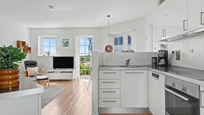 Et moderne køkken med hvide skabe, indbygget ovn og et spiseområde med tv og siddepladser.