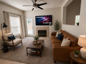 A living room with a sofa, armchair, coffee table, TV, fireplace, ceiling fan, and potted plants. - Modern Palm Springs Oasis - Heated Pool, Spa & Mountain View’s - Permit # 053440 (Palm Springs)